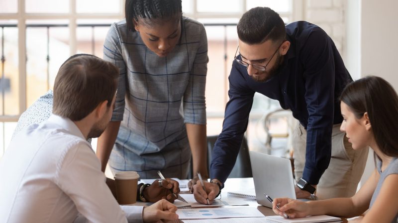 Focused multiracial corporate business team people brainstorm on marketing plan financial report gather at office table meeting, diverse serious colleagues group discuss paperwork engaged in teamwork