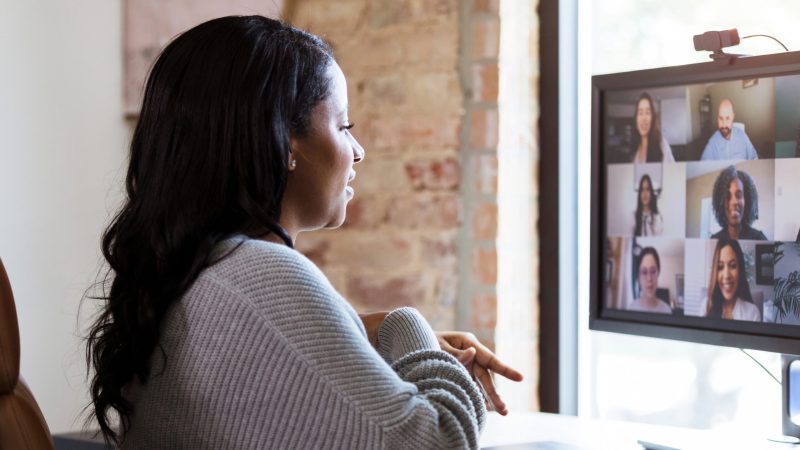 Since she has to work from home because of the coronavirus shutdown, the mid adult woman uses video conferencing to meet with her colleagues.